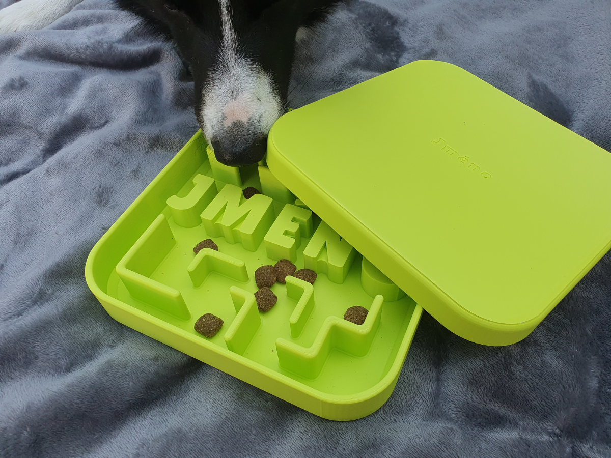 dog poking nose into medium size puzzle bowl partially covered by lid with kibble inside